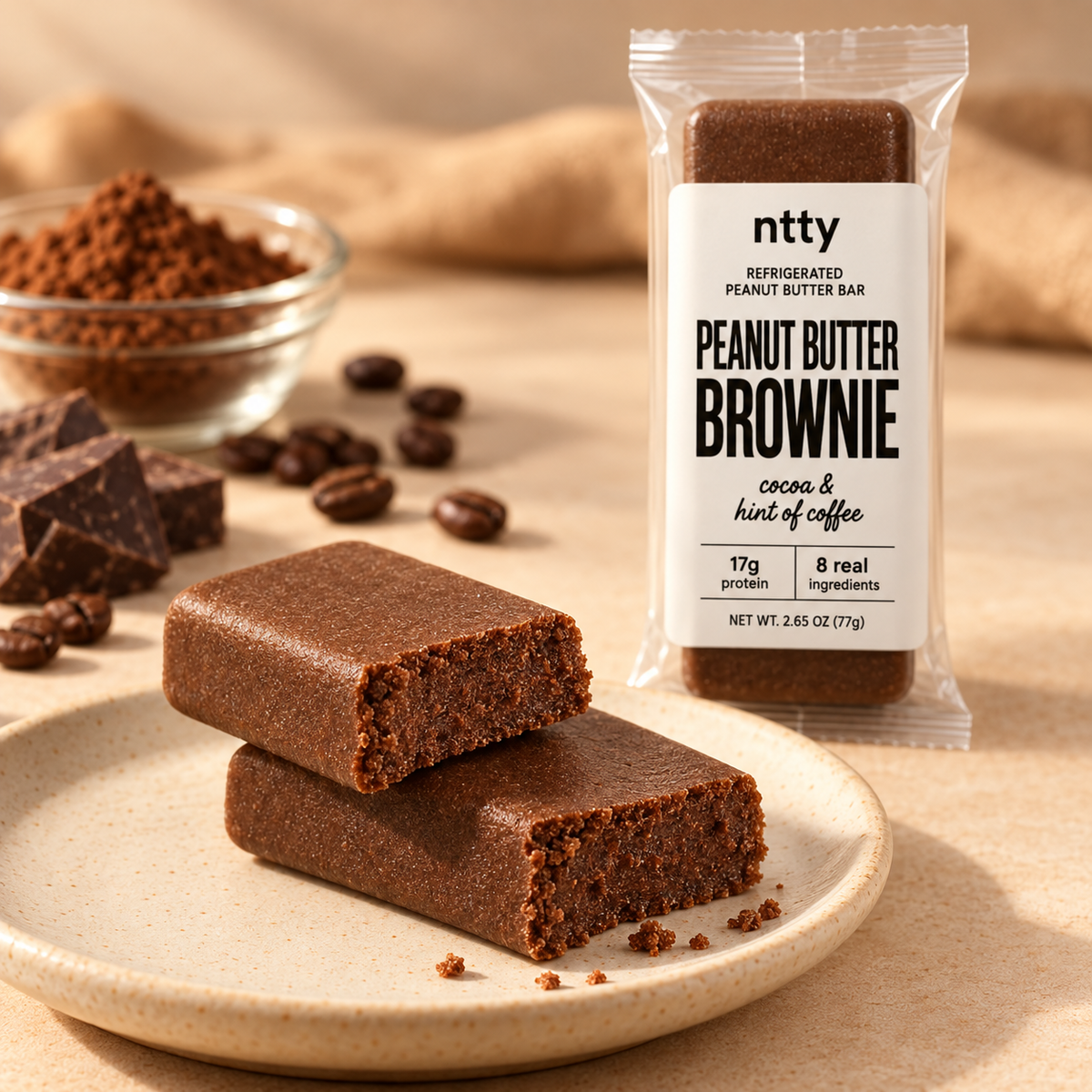 ntty brownie protein bar broken in half on a speckled plate, showing its soft, crumbly texture, with the wrapped bar behind it