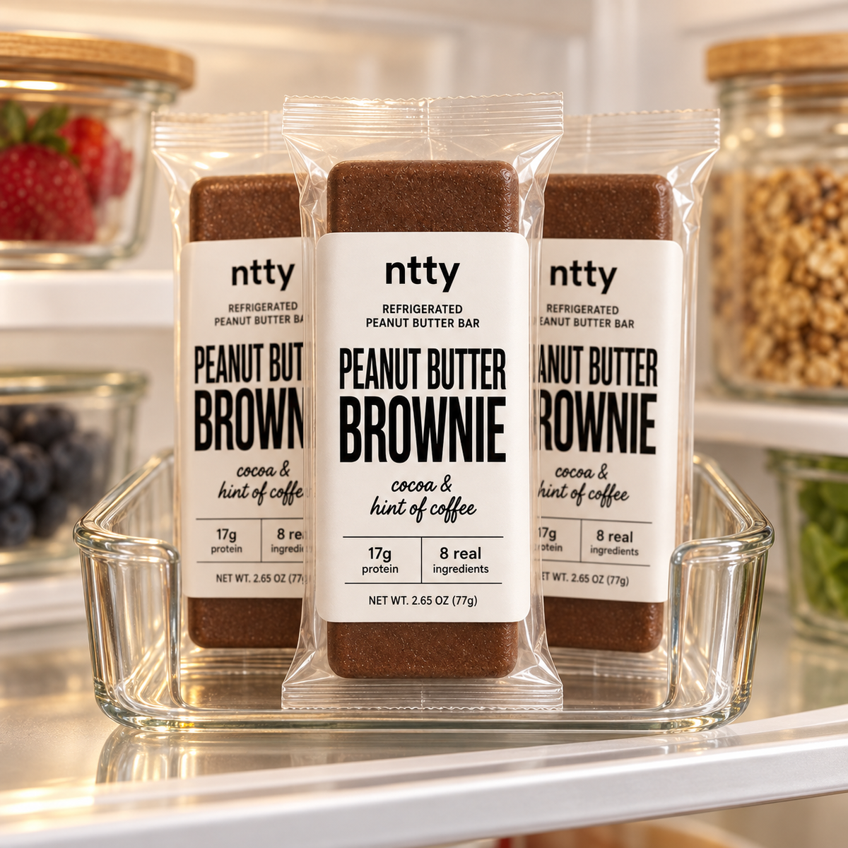 Three ntty brownie protein bars in a clear glass tray on a refrigerator shelf