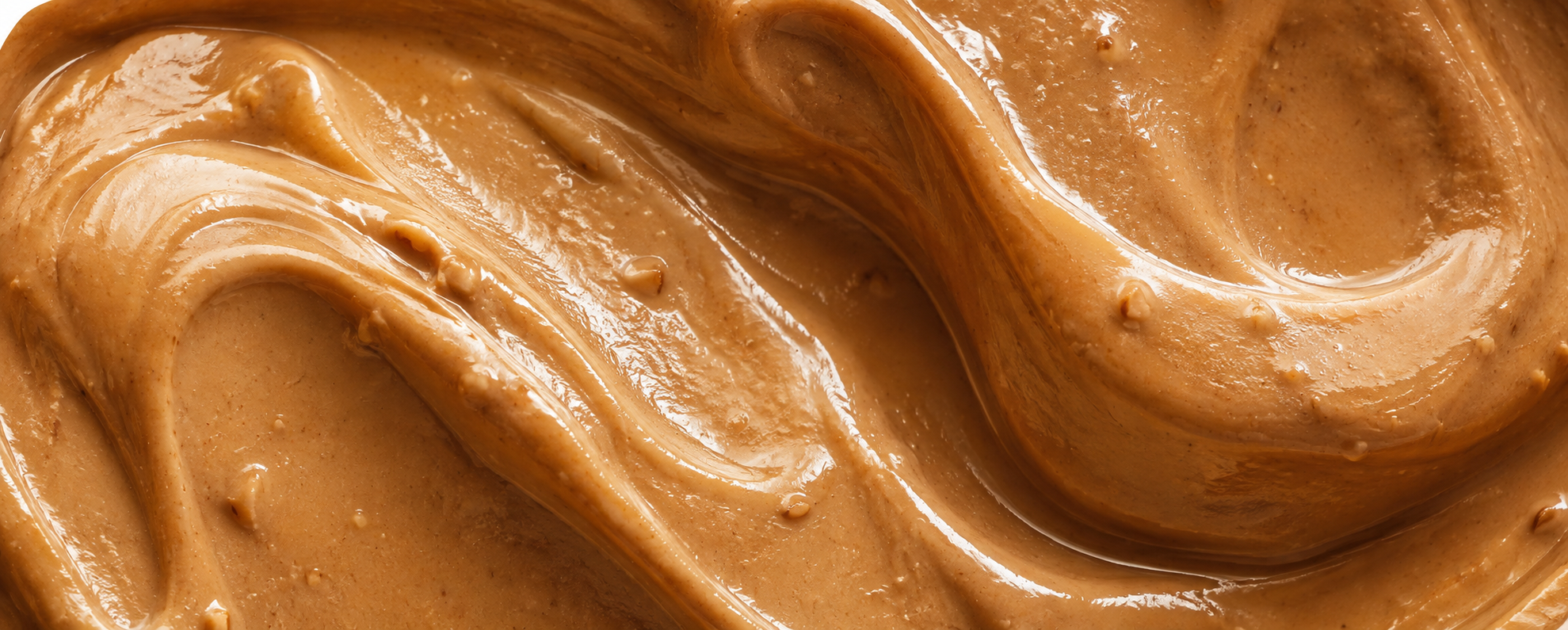 A close-up texture shot of smooth, creamy peanut butter with glossy highlights and visible peanut butter pieces, filling the entire frame.