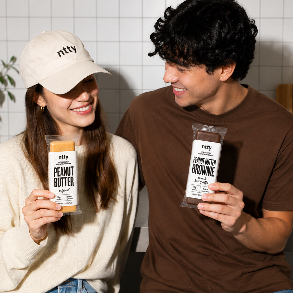 Couple in the kitchen holding a ntty peanut butter and peanut butter brownie refrigerated peanut butter protein bars.
