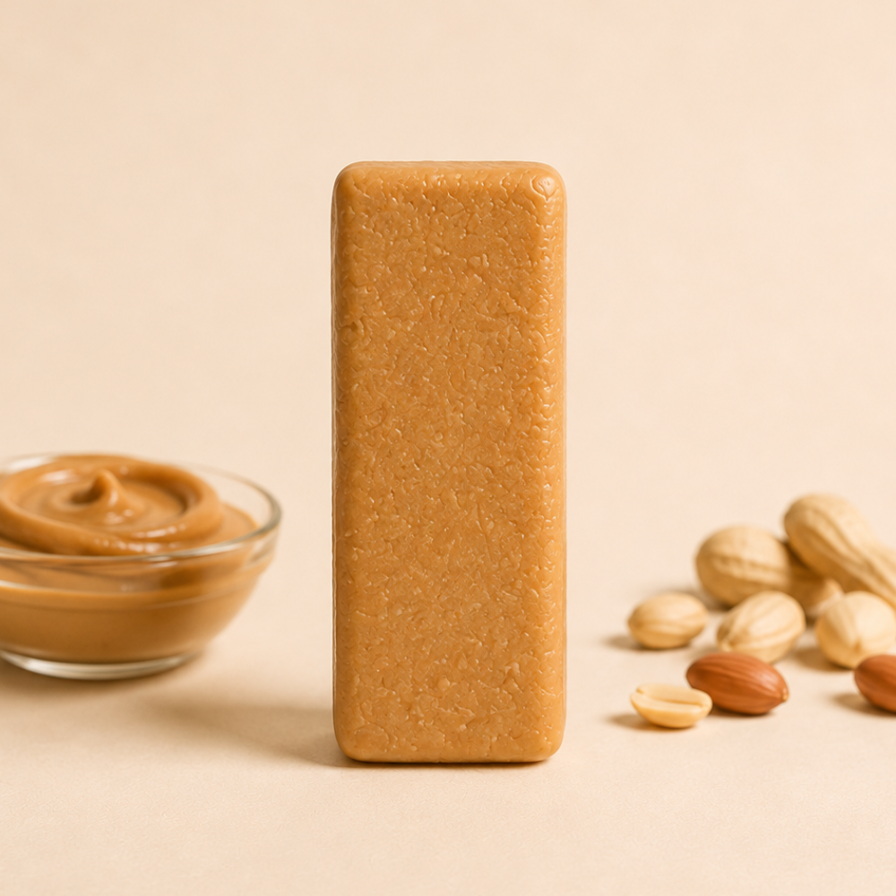 A unwrapped ntty refrigerated peanut butter bar with scattered peanuts and a bowl of creamy peanut butter.