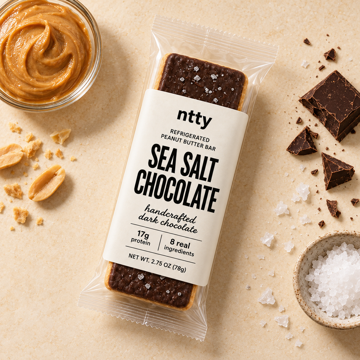 ntty sea salt chocolate protein bar surrounded by a bowl of peanut butter, handcrafted dark chocolate and sea salt