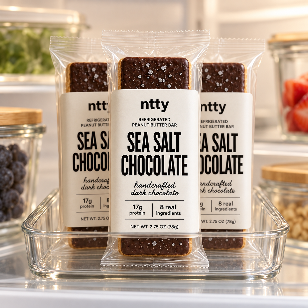 Three ntty sea salt chocolate protein bars in a clear glass tray on a refrigerator shelf