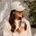 Woman holding a ntty peanut butter bar while wearing a white ntty cap outdoors.